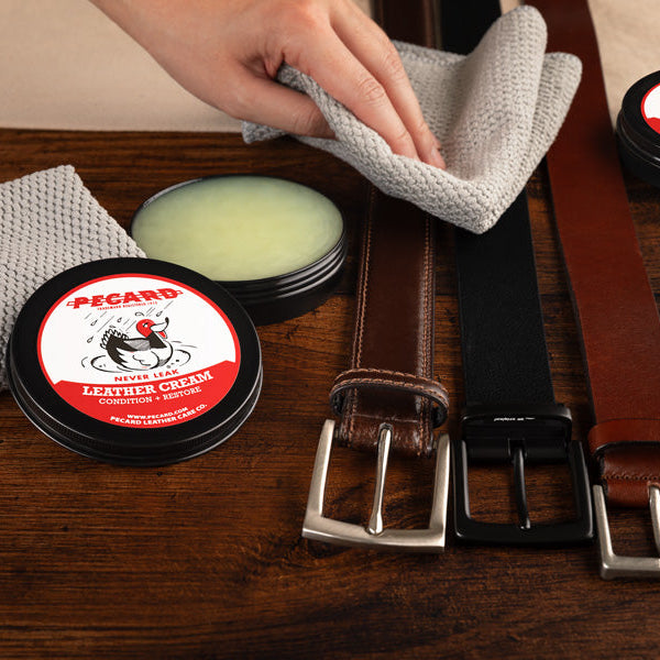 Leather care products including Pecard cream, cloths, and belts on a wooden surface with 'Pecard' branding.