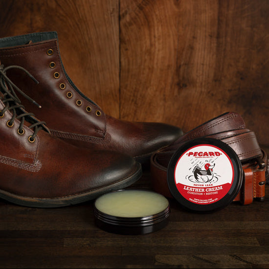 Brown leather boots with a jar of Pecard leather cream and rope on a wooden surface