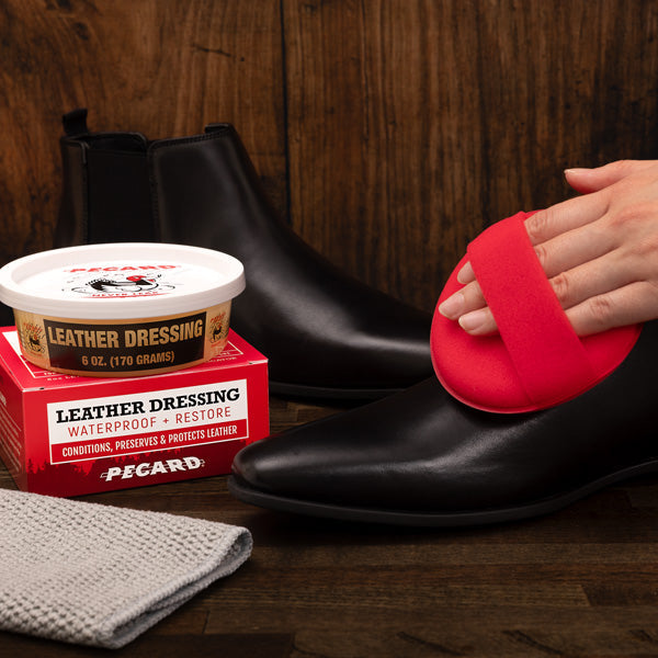 Person applying Pecard leather conditioner to a black shoe with Picard products in the background.